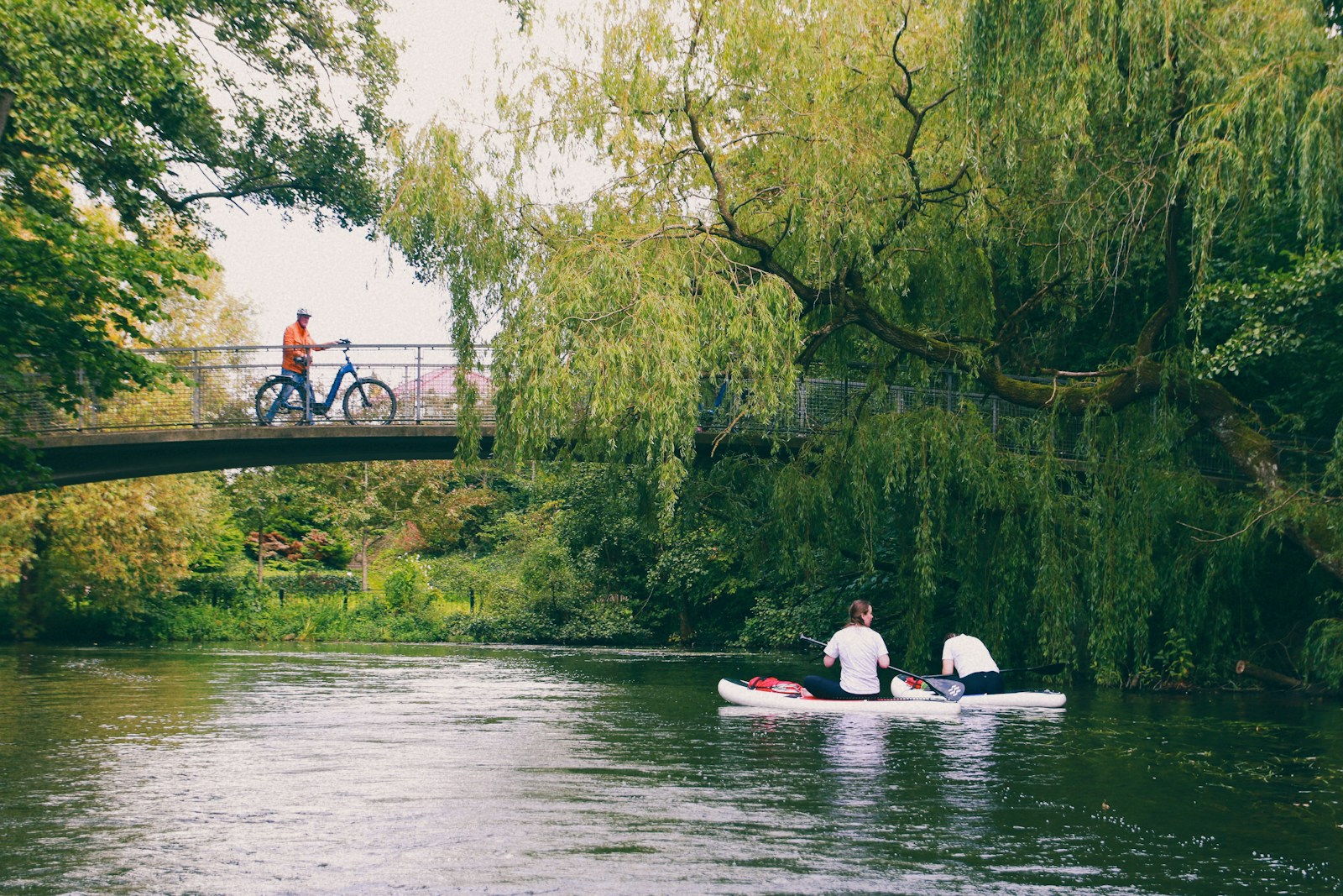 two people in a canoe on a river under a bridge